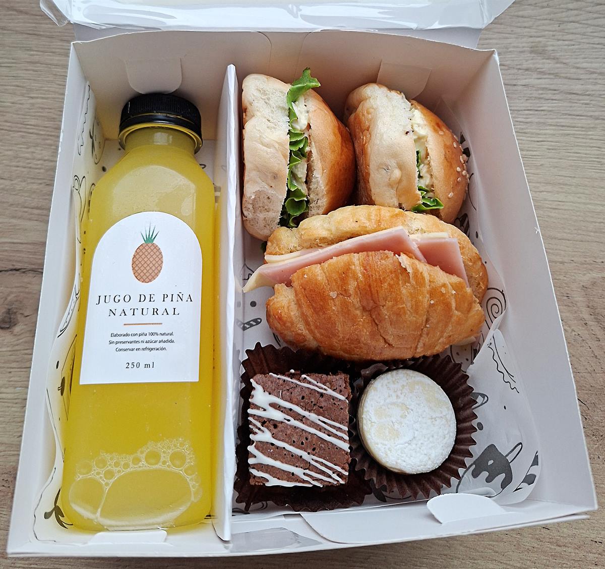 Box lunch corporativo con jugo de piña natural, sándwiches, croissant, brownie y alfajor