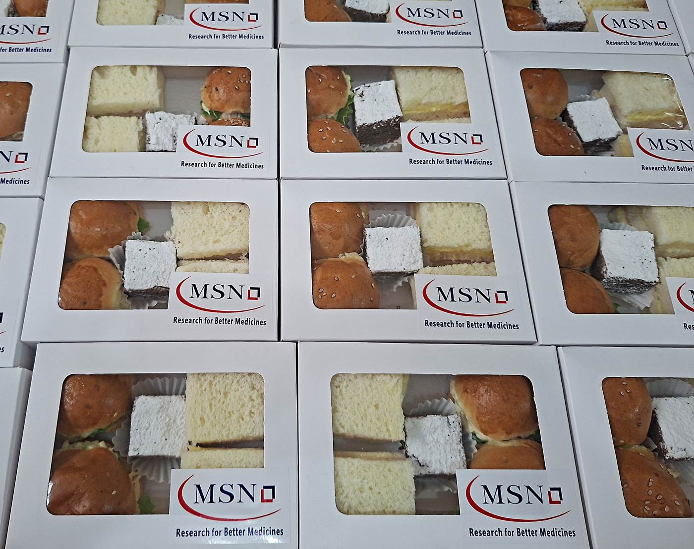 Cajitas de box lunch con visor y el logo de la empresa, con sándwiches, petipanes y brownie