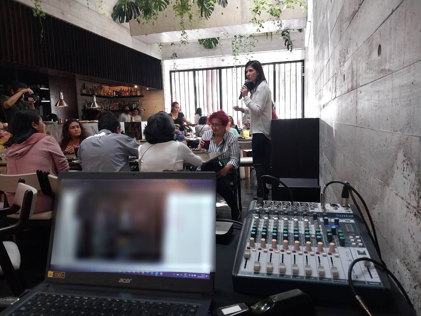 Consola de sonido y laptop controlando el audio de una presentadora con micrófono en un evento corporativo