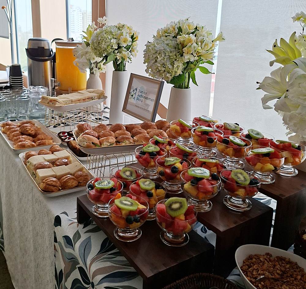 Paquete Premium de coffee break con copas de fruta, croissants, triples, jugo de naranja y café en una mesa decorada con flores
